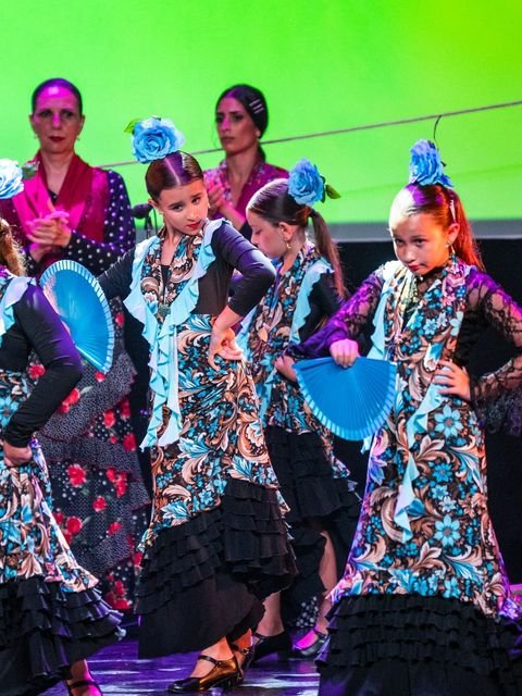 Alumnas de danza infantil bailando con abanicos azules bajo la luz verde del escenario