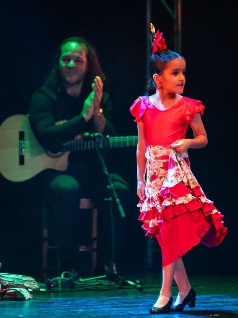 Alumna de pre-danza con traje rojo de volantes saliendo a escena, con el guitarrista al fondo